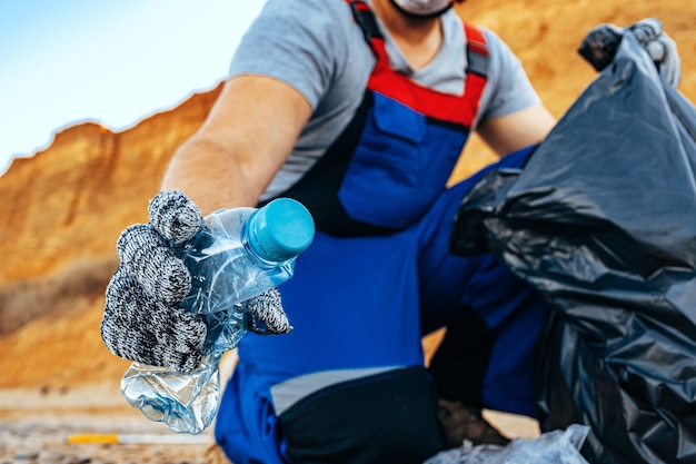 プラスチックごみをゴミ袋につかんでビーチを掃除するボランティアの男性の手がクローズアップ