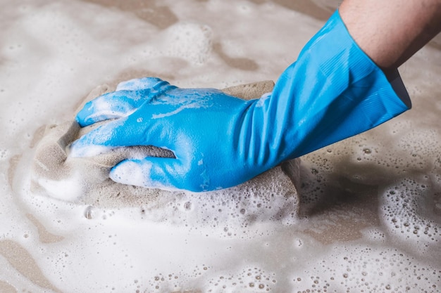 Photo hand of man wearing blue rubber gloves is using a sponge cleaning the tile floor