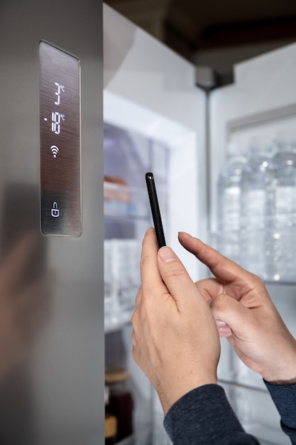 The hand of the man who controls the refrigerator with his smartphone. Internet of Things Concept.