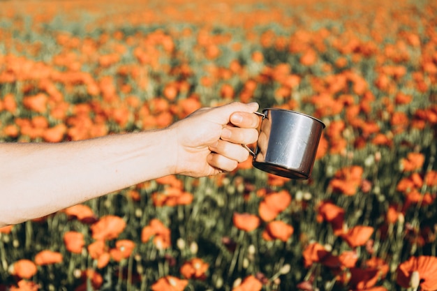 The hand of a man with a mug on a poppy field. positive\
emotions feeling life, peace of mind.