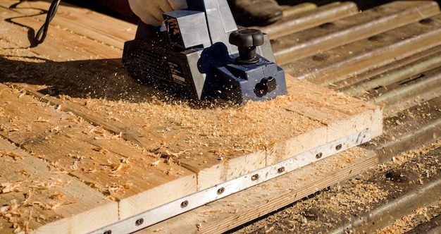 The hand of a man working with an electric planer and planed boards