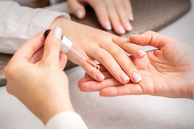 Mano di manicure versa l'olio con una pipetta alla cuticola delle unghie della giovane donna nel salone di bellezza