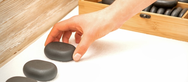 Hand of masseur lays out massage stones on the table