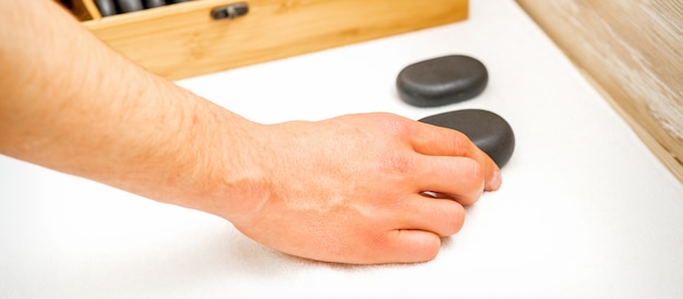 Hand of masseur takes black massage stones from the table in spa salon