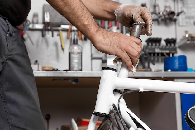 Hand mechanic in protective gloves putting bearing on bicycle pipe in workshop