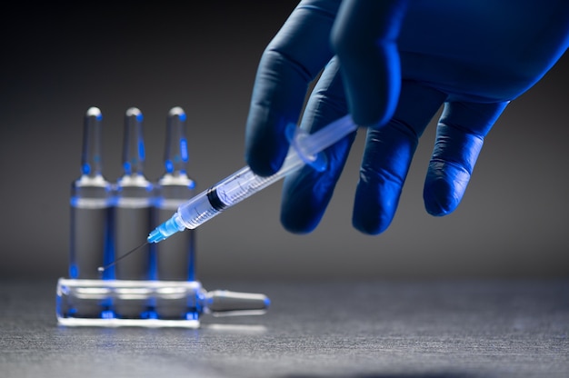 Hand in medical blue glove holding syringe over grey background.