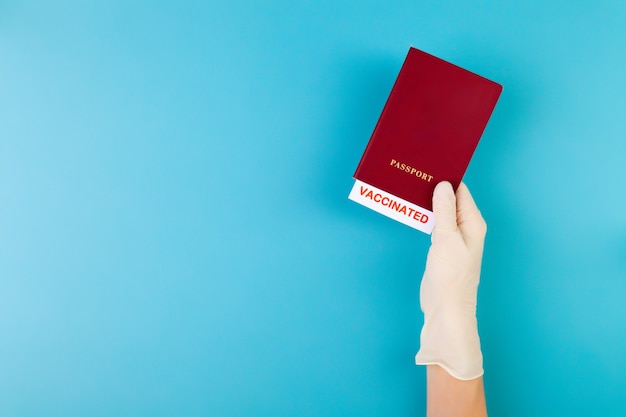 Hand in medical glove holding passport with vaccinated stamp on blue background