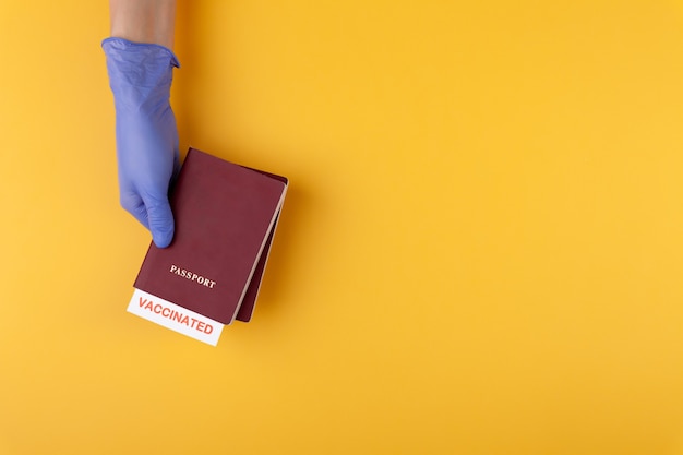 Foto mano in guanto medico con passaporto con timbro vaccinato su sfondo giallo