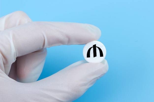 A hand in a medical glove holds a pill with a manat sign on a blue background Expensive medicine in Azerbaijan