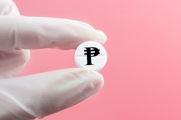 A hand in a medical glove holds a pill with a pesos sign on a pink background Expensive medicine in the Philippines Pharmaceutical business