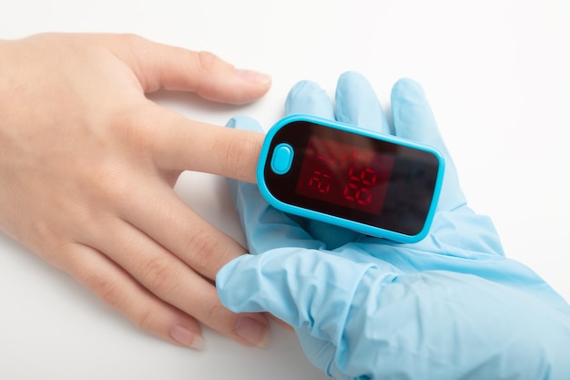 의료용 장갑을 낀 손은 특수 장치로 혈중 산소 포화도를 측정합니다.
