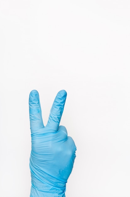 Рука в медицинской перчатке показывая знак победы на белой предпосылке. Жест победы. Копировать пространство