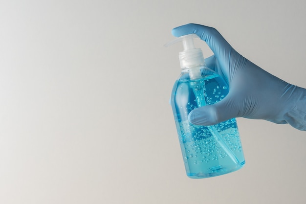 Hand in medical glove with hand sanitizer in a bottle on white background