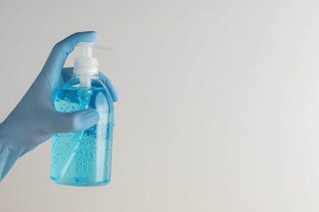 Hand in medical glove with hand sanitizer in a bottle on white.