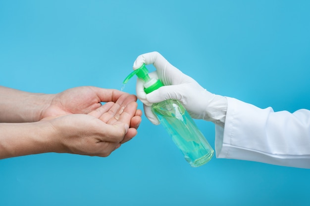 Photo hand in medical gloves applying sanitizer gel onto men hands for protection against infectious virus, bacteria and germs in blue wall