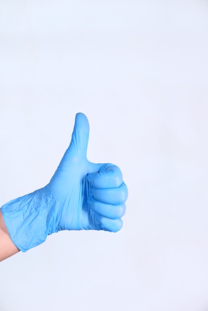 hand in medical gloves showing a thumb-up on white wall