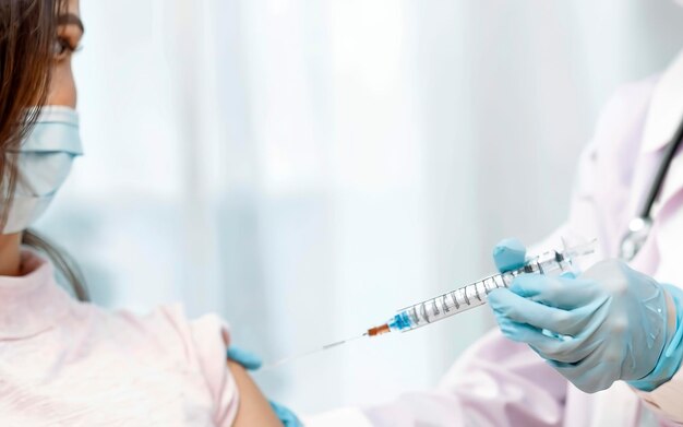 hand of a medical worker with an injection syringe prepares to be vaccinated in the shoulder