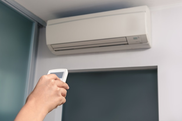 Hand met afstandsbediening gericht op de airconditioner in de kamer