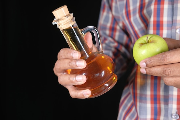 Hand met appelazijn in glazen fles met verse groene appel