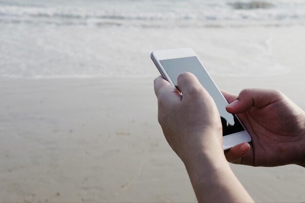 Hand met behulp van slimme telefoon op het strand