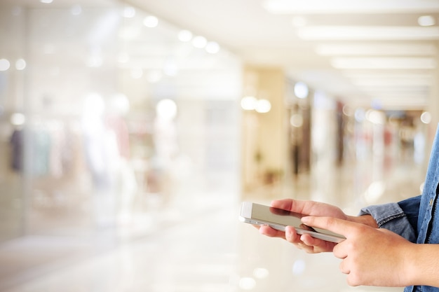 Hand met behulp van slimme telefoon over onscherpte winkel met bokeh lichte achtergrond