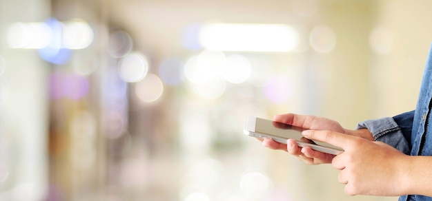 Hand met behulp van slimme telefoon over onscherpte winkel met bokeh lichte achtergrond