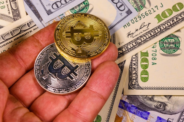 Foto hand met bitcoins tegen de honderd dollar biljetten