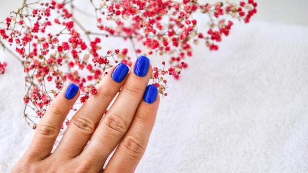 Hand met blauwe nagels op gedroogde bloemen achtergrond. vrouwelijke manicure. glamoureuze mooie manicure. winter- of herfstmanicure in blauw. modieuze nagellak kleur nagellak
