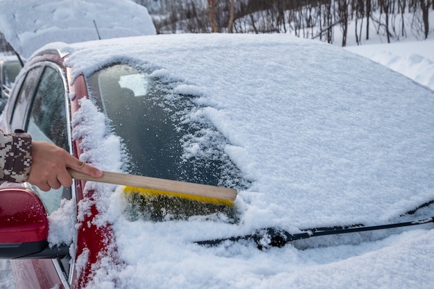 Hand met borstel sneeuw vegen op de voorruit van de auto in de winter