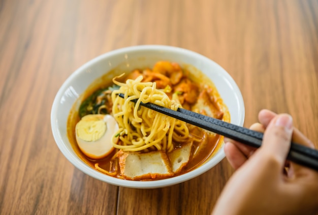 Hand met Chinese eetstokjes die noedel eten