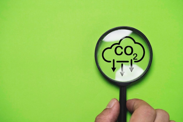 Hand met CO2-reducerend pictogram in vergrootglas om scherp te stellen, CO2- of kooldioxide-uitstoot te verminderen, koolstofvoetafdruk en koolstofkrediet om de opwarming van de aarde door het concept van klimaatverandering te beperken