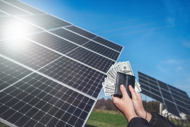 hand met dollarbiljetten die uit een portemonnee zien op een achtergrond van zonnepanelen