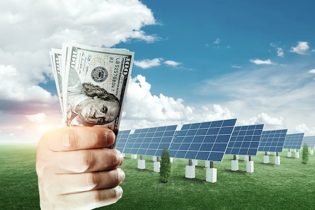 Hand met dollars op de achtergrond van zonnepanelen... Zonne-energiezaken, de kosten van groen