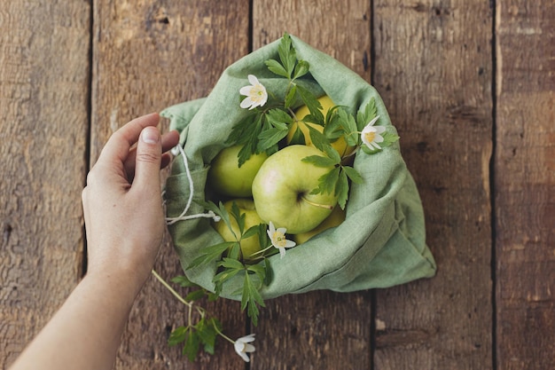 Hand met eco-katoenen tas met verse appels en bloemen op rustiek hout Zero waste shopping