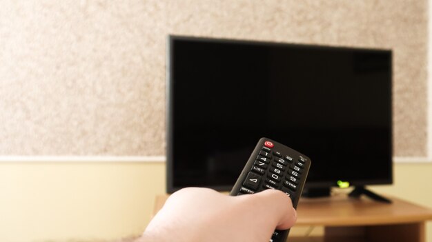 Hand met een afstandsbediening van de televisie en surfen op programma's op televisie. kijk, zet de tv aan of uit in de woonkamer of slaapkamer op het nachtkastje met zwart scherm. Ruimte kopiëren.