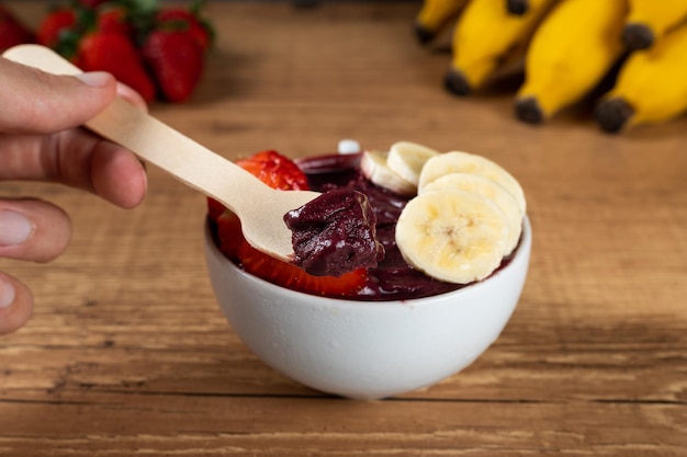 Hand met een Braziliaanse Acai Bowl met banaan en aardbei op een houten achtergrond