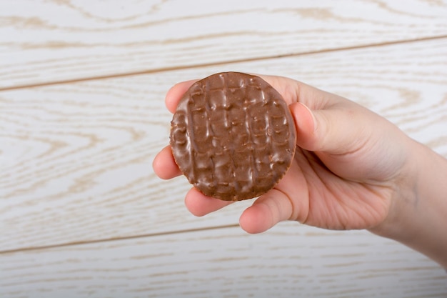 Hand met een chocolade bedekt koekje op een houten achtergrond