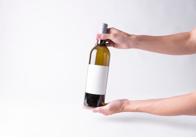 Hand met een fles wijn voor mock-up. Leeg etiket op een grijze achtergrond.