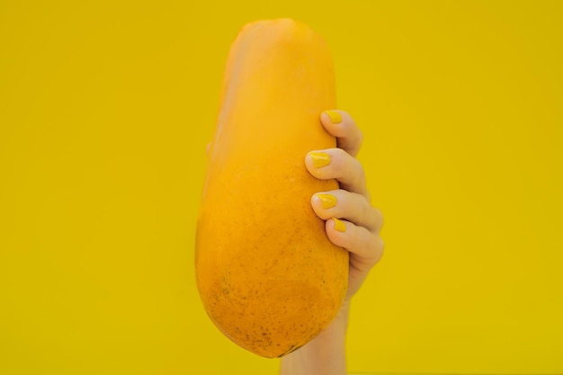 Hand met een gele manicure met een oranje rijpe papaja op een gele achtergrond