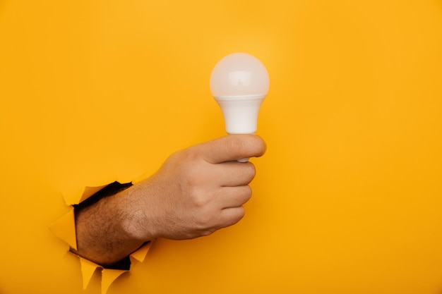 Hand met een gloeiende led-lamp uit een gescheurd gat in geel papier