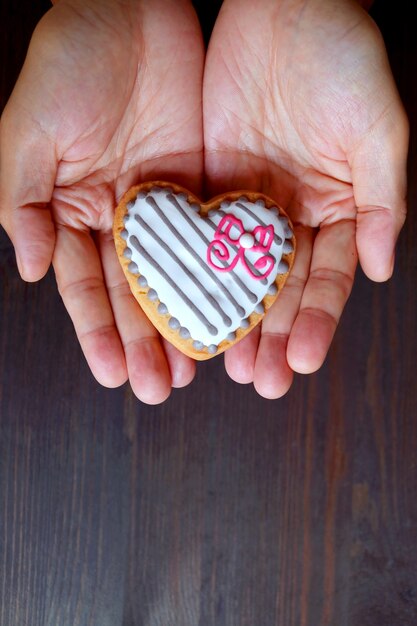 Hand met een hartvormige witte chocolade geglazuurde cookie op donkerbruine houten achtergrond