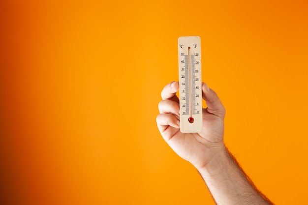 Hand met een huisthermometer. luchttemperatuur op een oranje achtergrond