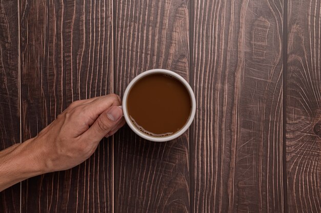 Hand met een koffiemok op een houten achtergrond