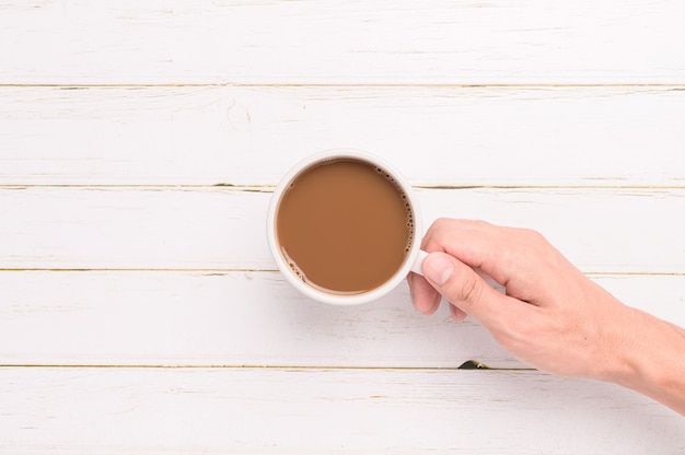 Hand met een koffiemok op een houten ondergrond