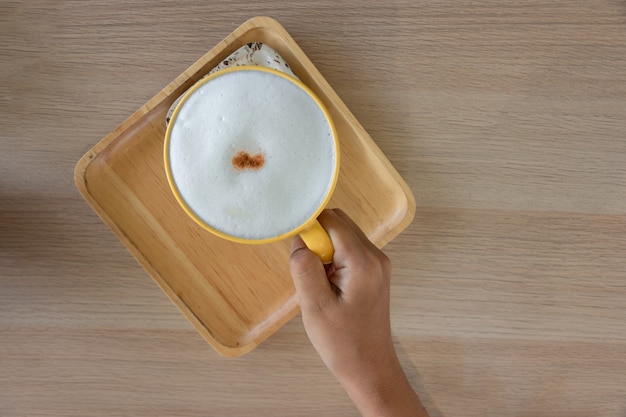 Hand met een kopje cappuccino koffie met schuim op houten tafel