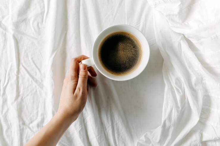 Foto hand met een kopje zwarte koffie op wit laken ontbijt op bed concept