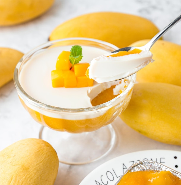 Foto hand met een lepel schepte de mango pudding op mango pudding topping met verse rijpe mango gesneden dobbelstenen vorm en munt in glazen kom op een marmeren tafel taart in café of bakkerij winkel