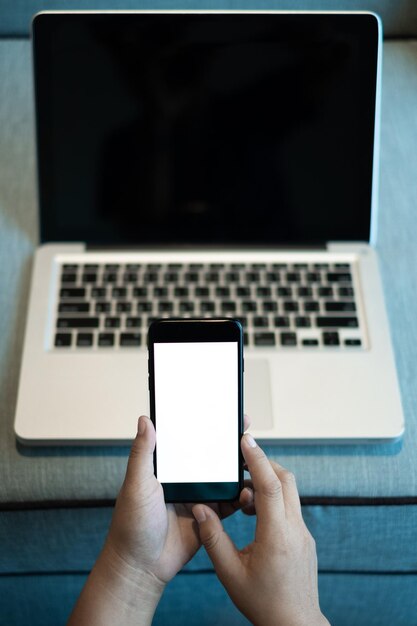 Hand met een mobiele telefoon met een wit leeg scherm over de laptop