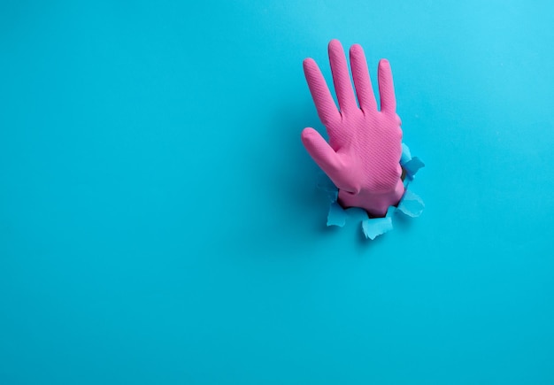 Foto hand met een open handpalm steekt uit een gescheurd gat in blauw papier met gebaren om te stoppen