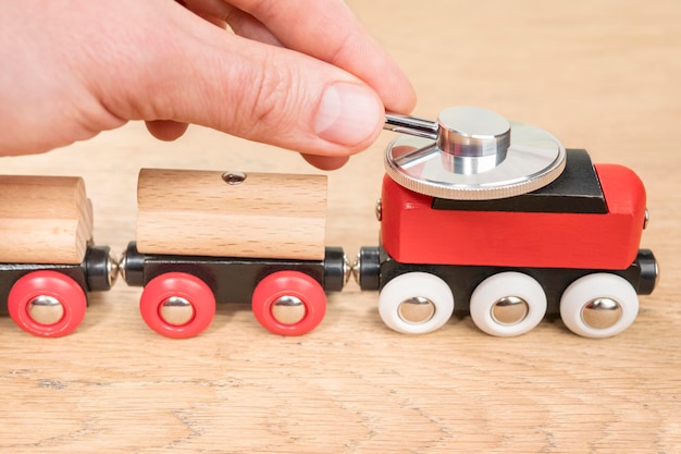 hand met een phonendoscope op het dak van de locomotief van een speelgoedtrein die op een houten tafel staat
